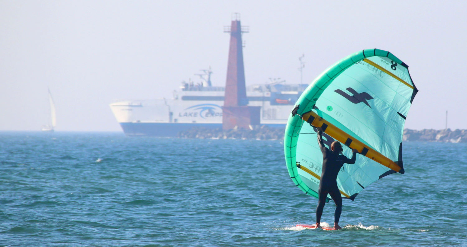 A wing foiler rides with a large, light wind wing.