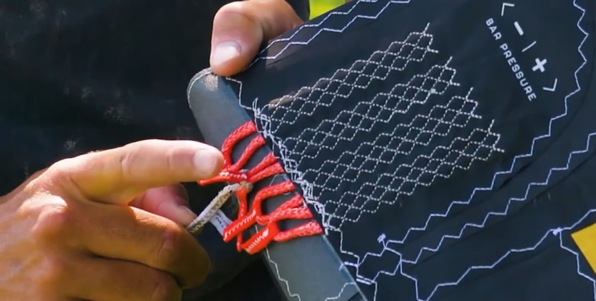 Connect your line to the point closest to the edge of the wingtip for lighter bar pressure and faster turning. A kiteboarder points to the adjustment points on the kite's wingtip.