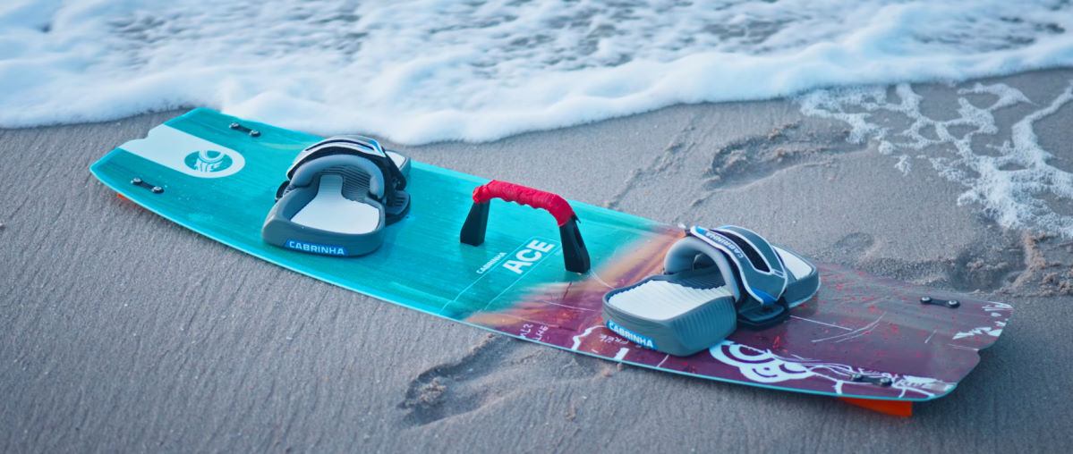 The 2025 Cabrinha Ace kiteboard sites on the beach as a wave washes up near it.