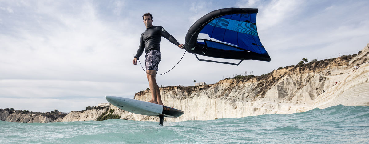 A wing foiler rides on the Quest foilboard.