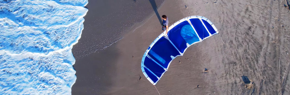Drone view of a kiteboarder walking toward the water with a 2026 Cabrinha Switchblade kite.