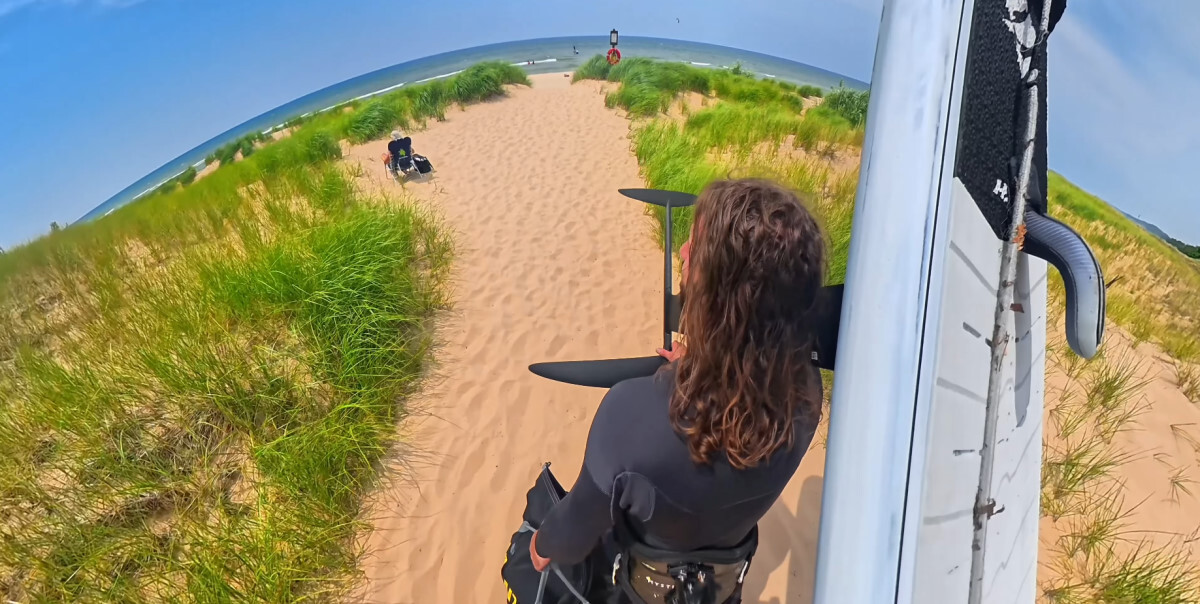 Tucker walking across the beach with his wing foiling gear.