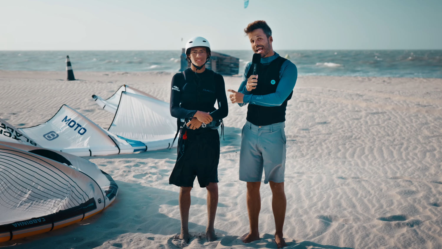 Both kites are great options, but which is right for you? Rubens and Kauan stand on the beach beside the Moto Apex and Switchblade Design Works kites.