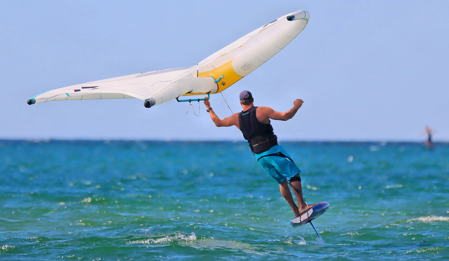 A wing foiler holds a wing with a boom over his head as he turns.
