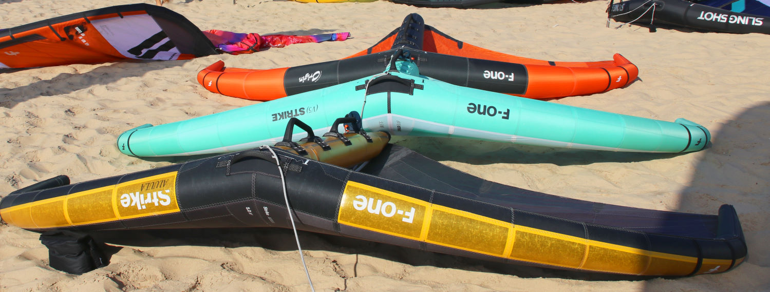 Three F-One wings sit on the beach.