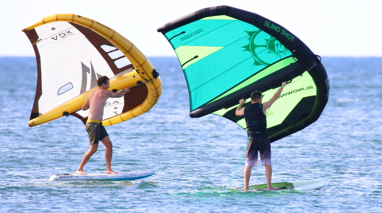 Two wing foilers ride on the lake. One wing has windows and the other does not.