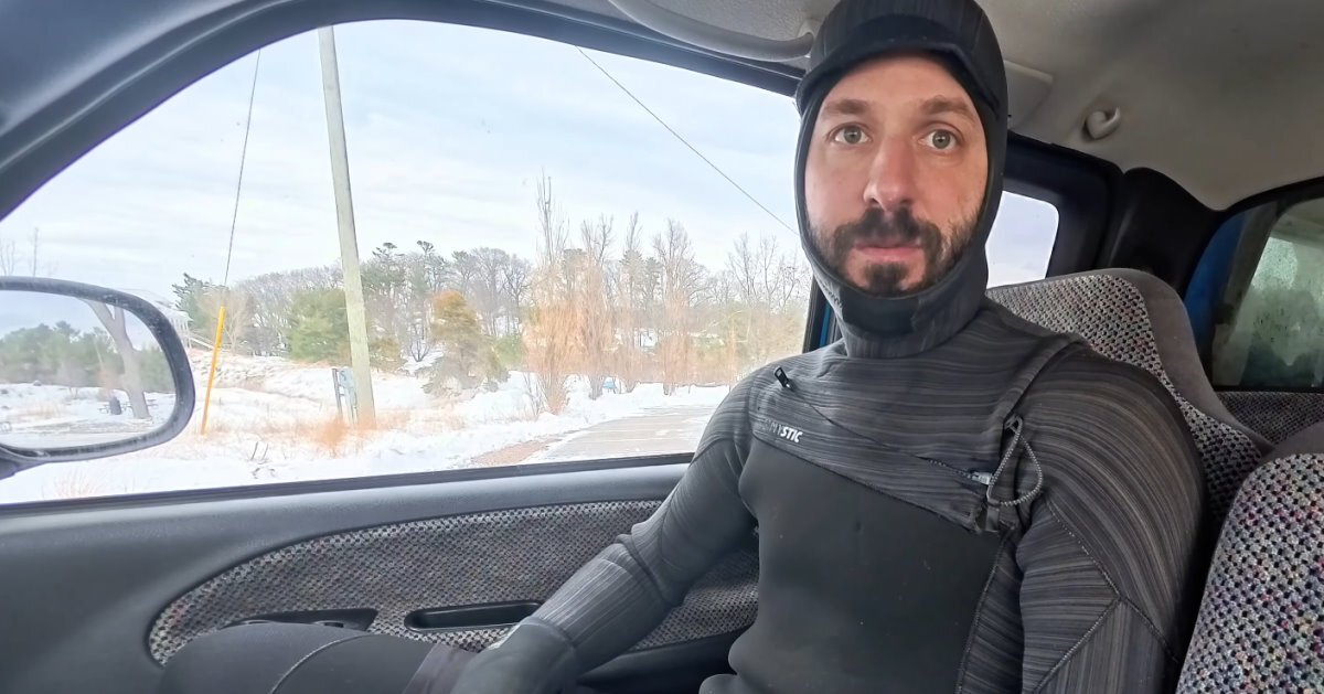 Tucker sits in his truck wearing a wetsuit with a hood attached.