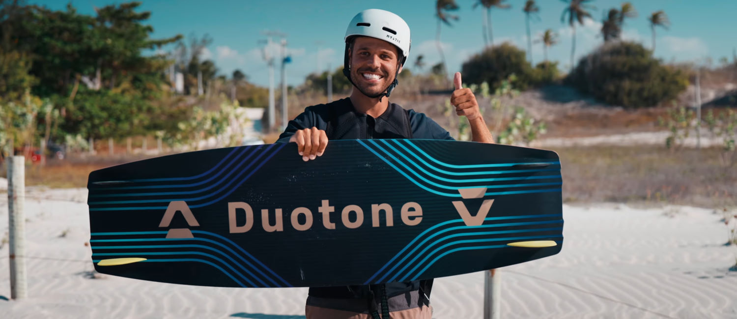 Rubens gives a thumbs-up as he holds up the Duotone Jaime SLS twintip board, showing its bottom side.