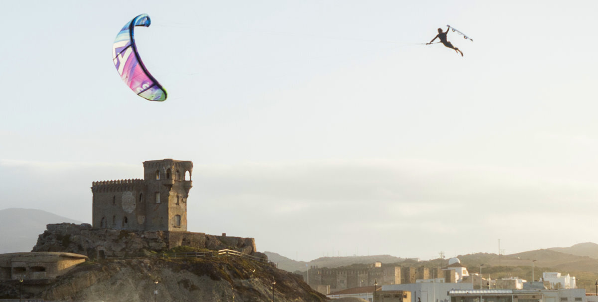 A kiteboarder jumps while holding their board in their hand with a castle in the background.