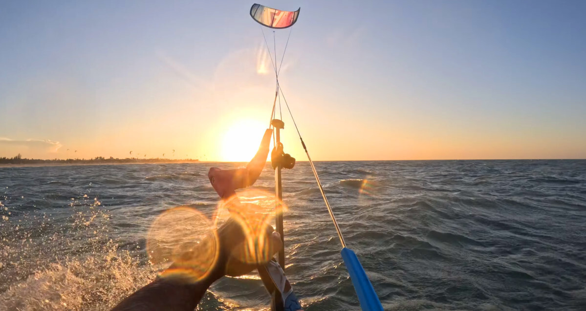 A kiteboarder pull hard on the bar to make the kite turn fast as the sun sets ahead of him.