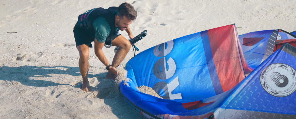 Sand is free and plentiful at most launch sites. A kiteboarder tosses sand on his kite to hold it down.