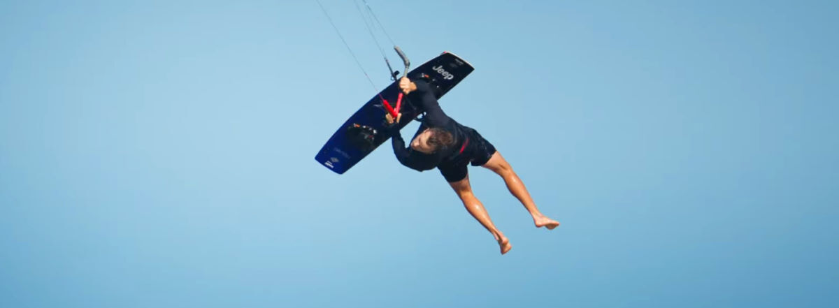 Stig jumps, holding his Naish Drive board.