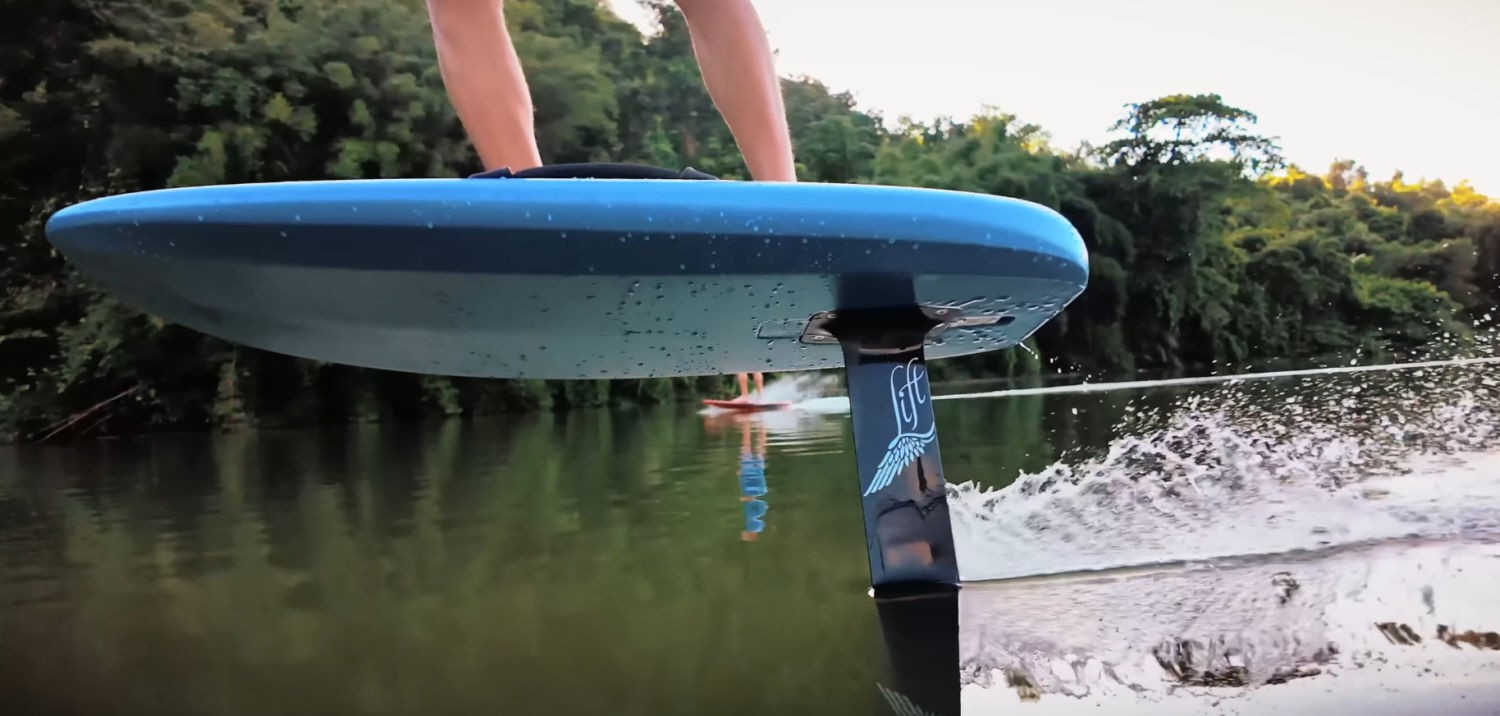 The full carbon setup makes the Lift5 much lighter weight. A foiler stands on the Lift5 board, with the mast just visible out of the water.