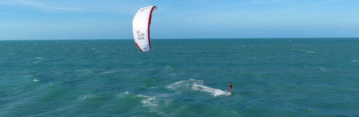 Nick created the Yes kite to help the next generation of riders achieve their goals. A kiteboarder rides across the water with a Jacobsen Yes kite.