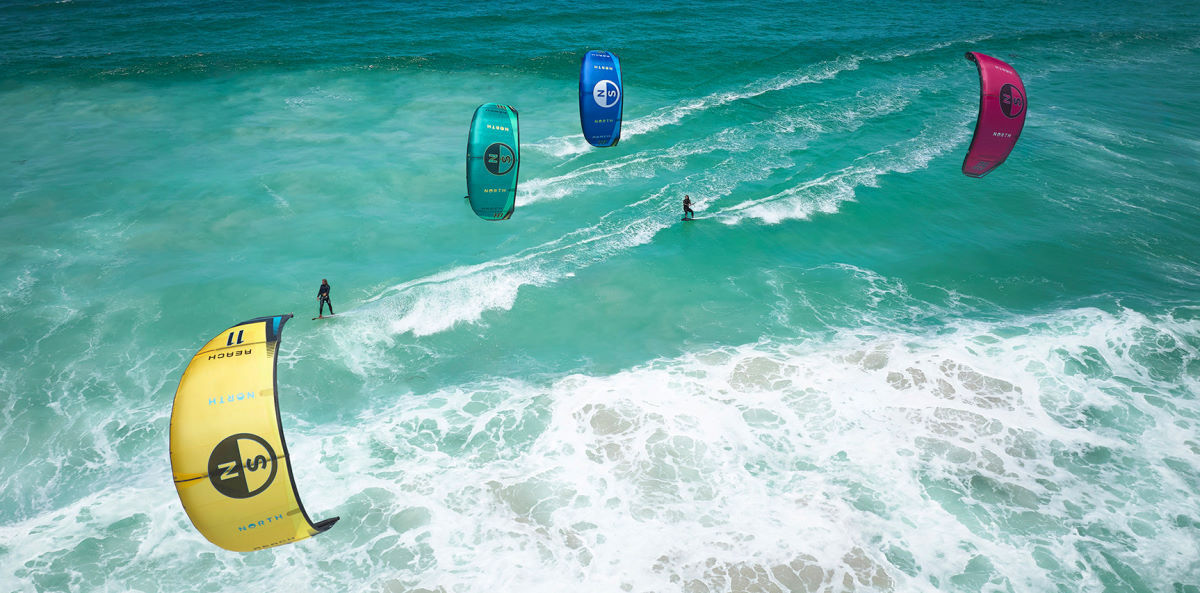Four kiteboarders ride in a line with Reach kites.