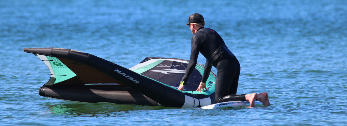 Jeff uses his wing to steady himself while climbing onto his board.