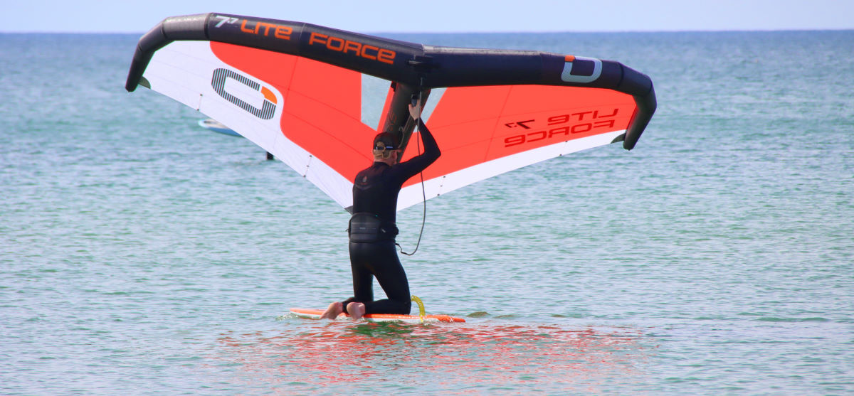 Jeff kneels on his wing foilboard, facing sideways.
