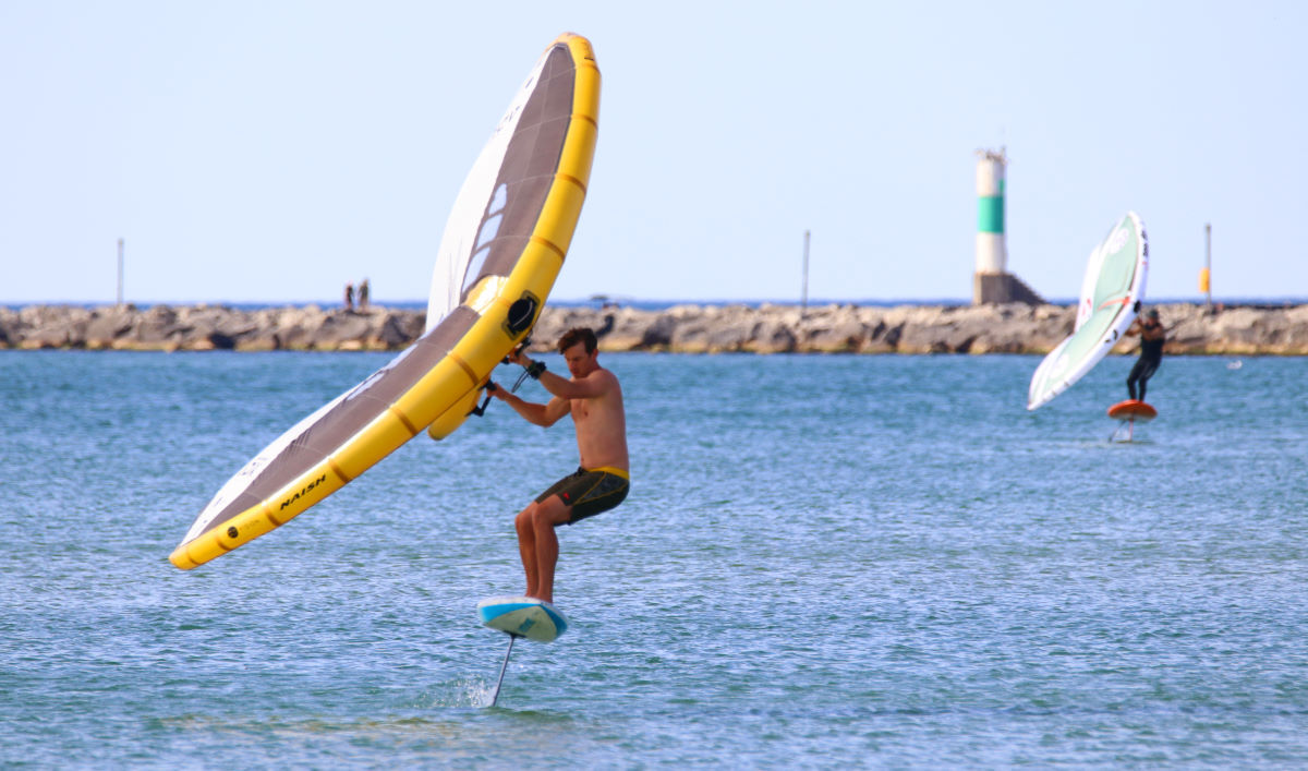 A wing foiler pumps his board, using a narrow stance.