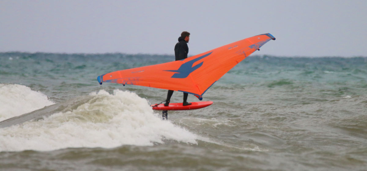 A wing foiler rides a wave, using a wide stance.