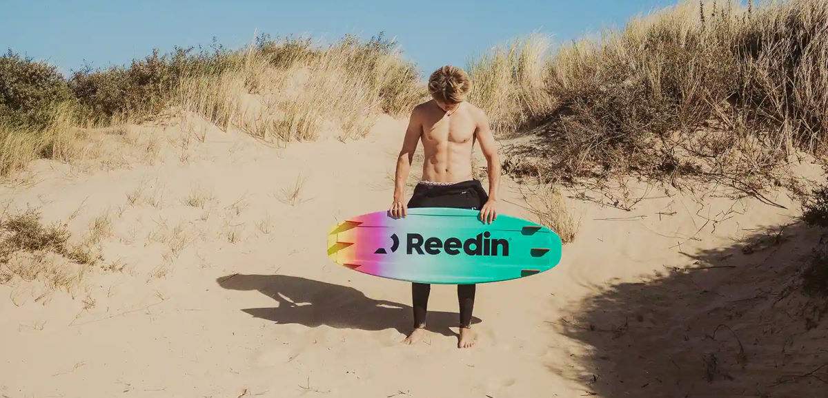 A kiteboarder stands at the base of a dune, holding the SnackPack board.