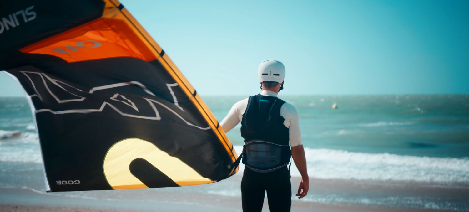 Wind? Check. Kite? Check. It's time to ride! Rubens stands on the beach, ready to enter the water with the Slingshot Code NXT V2 kite.