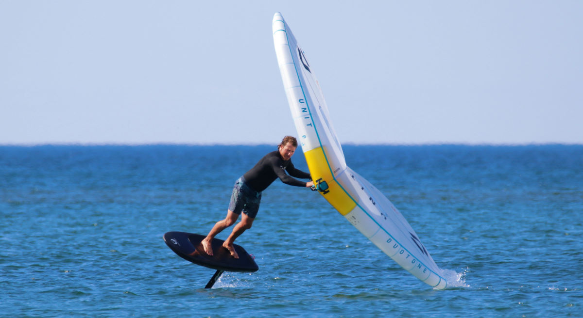 A wing foiler makes a toeside turn, dragging his wingtip in the water.