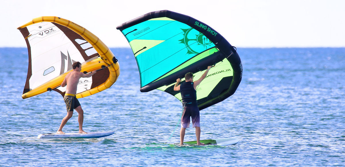 Two wing foilers ride, one heelside and one toeside on the board.
