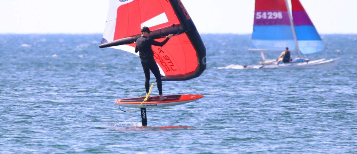 Our goal is to help you neet your goals for fun on the water! Jeff wing foiling with a sailboat in the background