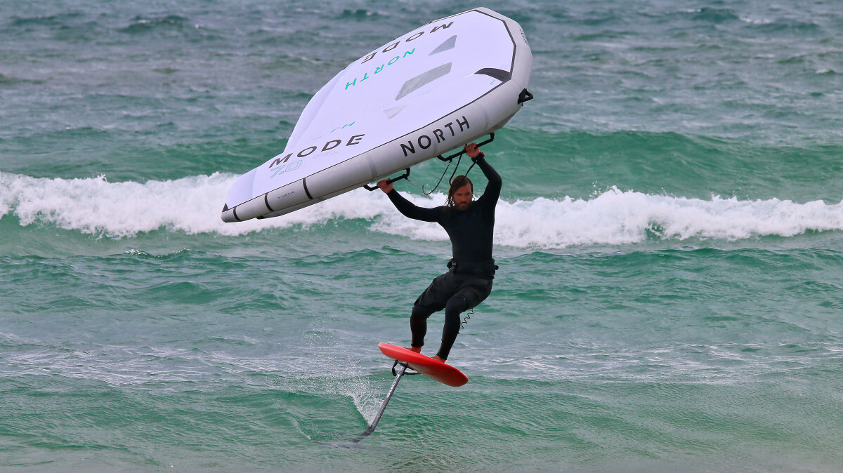 Use the wing for a little extra lift. Tucker wing foiling on a small wave and holding the wing over his head